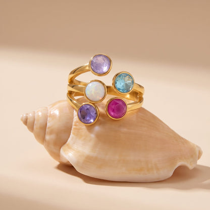 The Isabella rainbow stone gold ring resting on a seashell