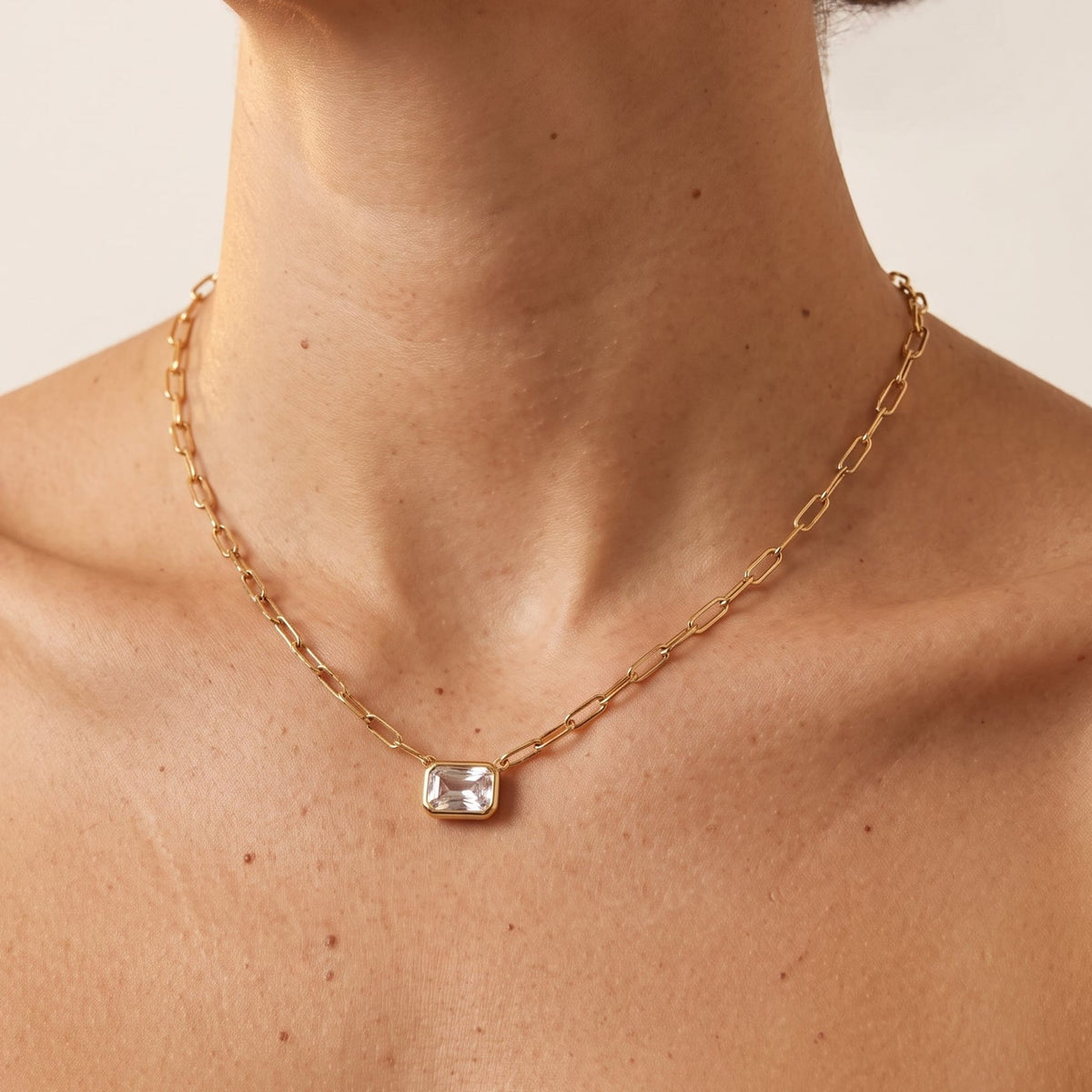 Woman wearing the Isabelle emerald cut gold necklace at the collarbone, featuring a rectangular crystal pendant