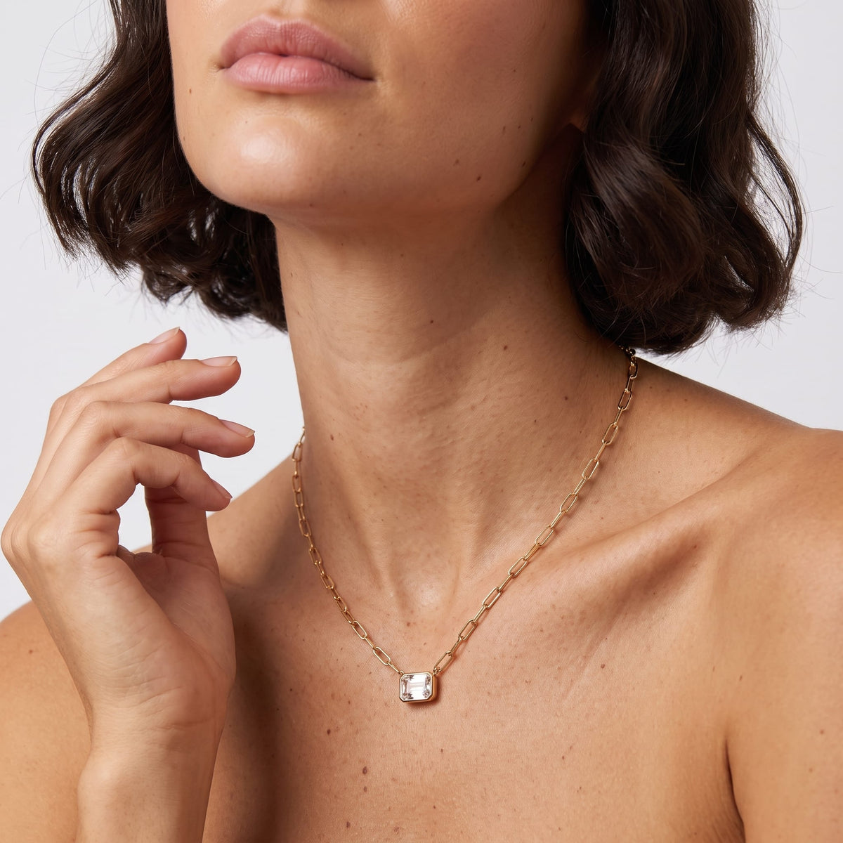 Woman wearing the Isabelle emerald cut gold necklace at the collarbone with hand raised