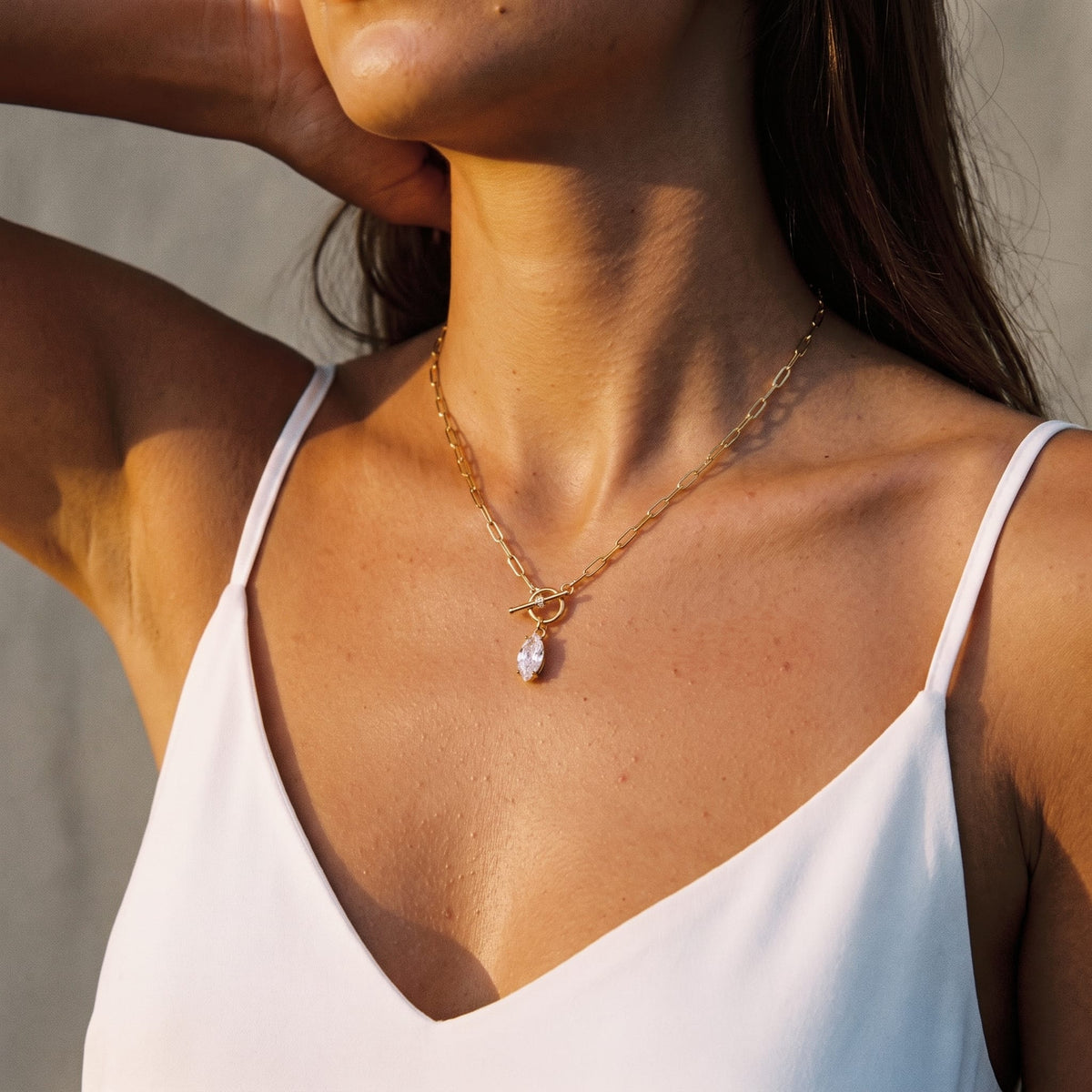 Woman wearing the Isabelle marquise toggle gold necklace at the collarbone in warm evening light