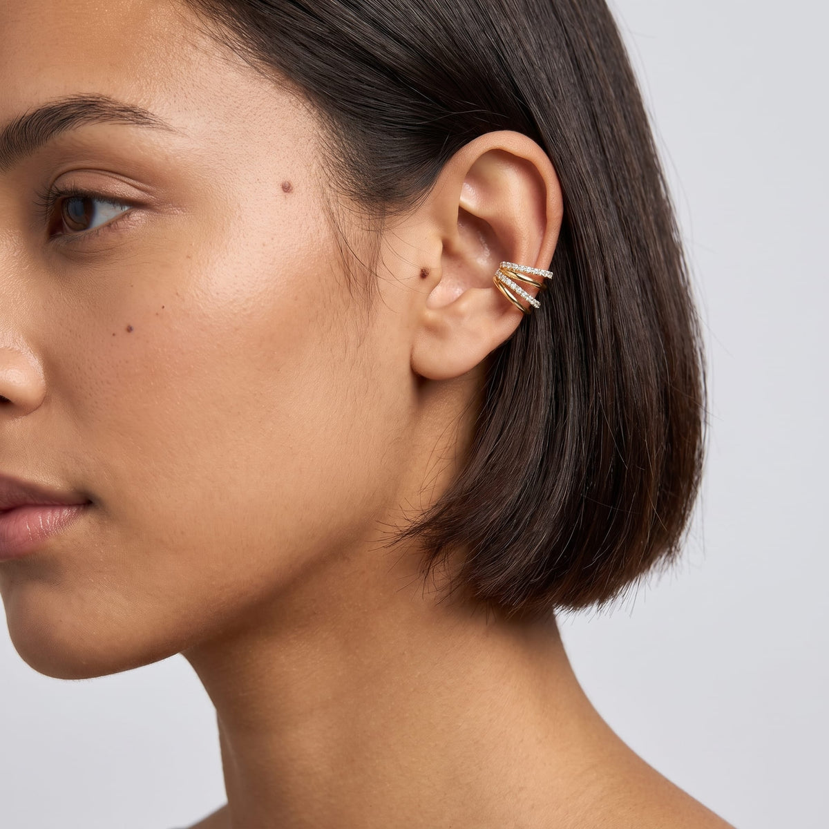 Woman wearing the Jeanne crisscross gold ear cuffs on the ear, featuring short dark hair