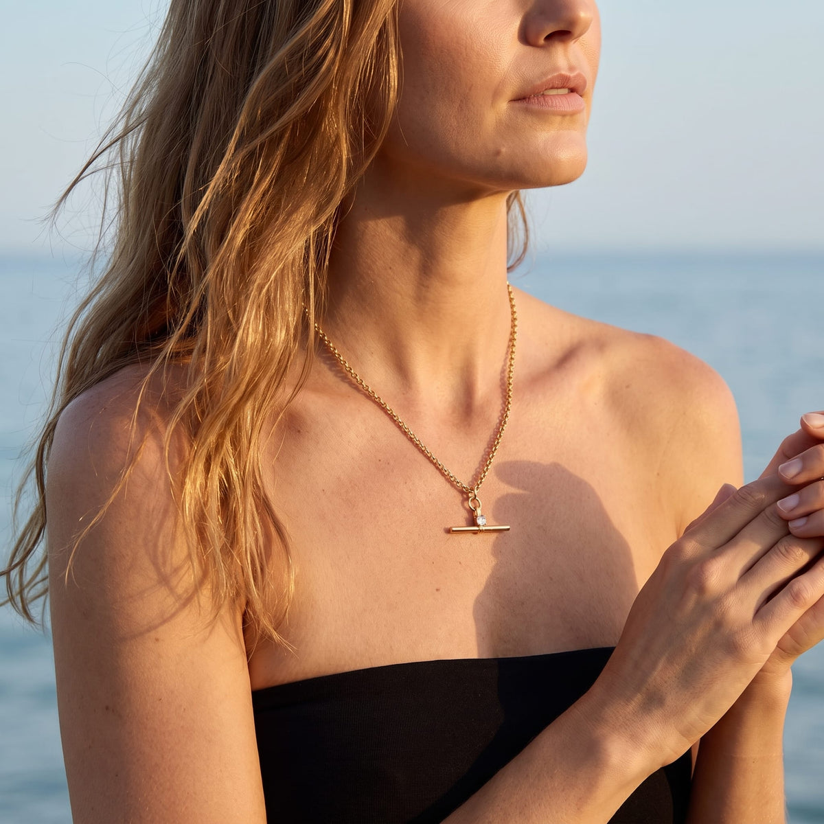 Woman wearing the Joséphine t-bar crystal gold necklace at the collarbone in front of the sea