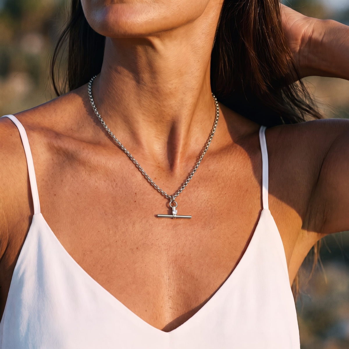 Woman wearing the Joséphine t-bar crystal silver necklace at the collarbone with hand in hair