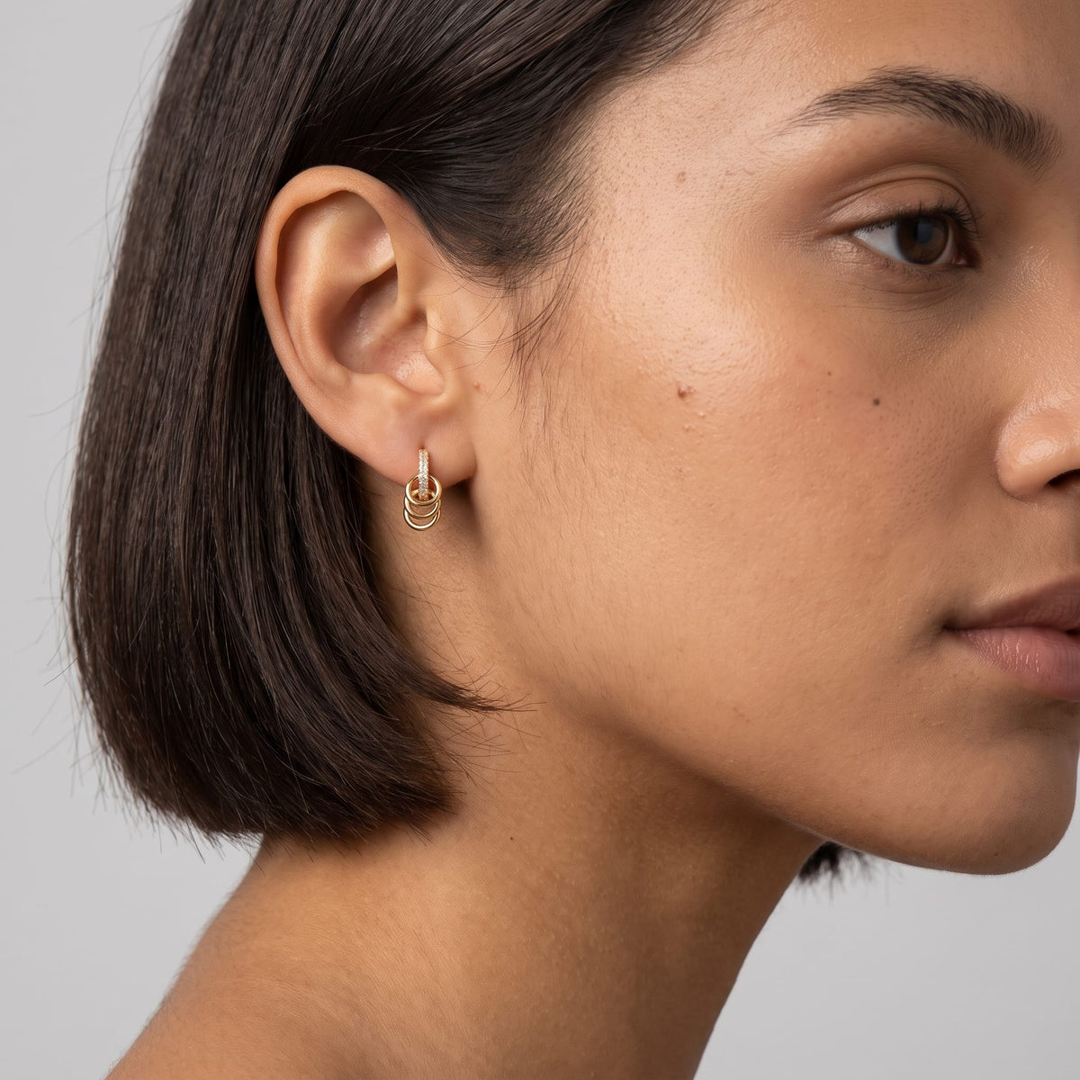 Woman wearing the Joséphine triple loop gold earrings on the ear featuring a short dark hairstyle