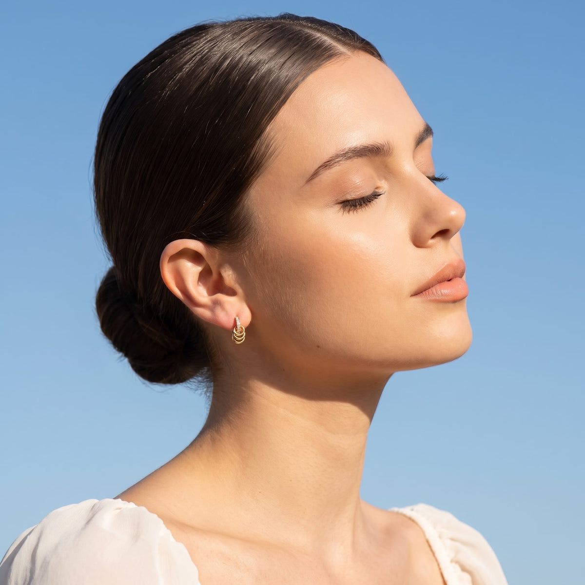 Woman wearing the Joséphine triple loop gold earrings on the ear posing under a bright blue sky