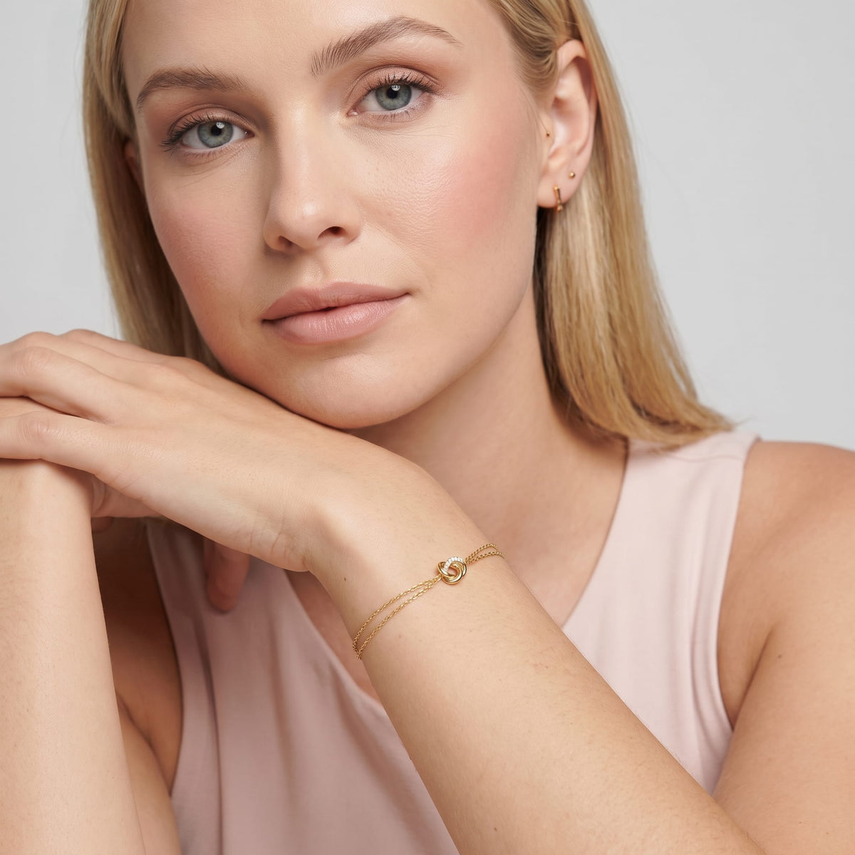 Woman wearing the Juliette love knot gold bracelet on the wrist while resting her chin on her hands