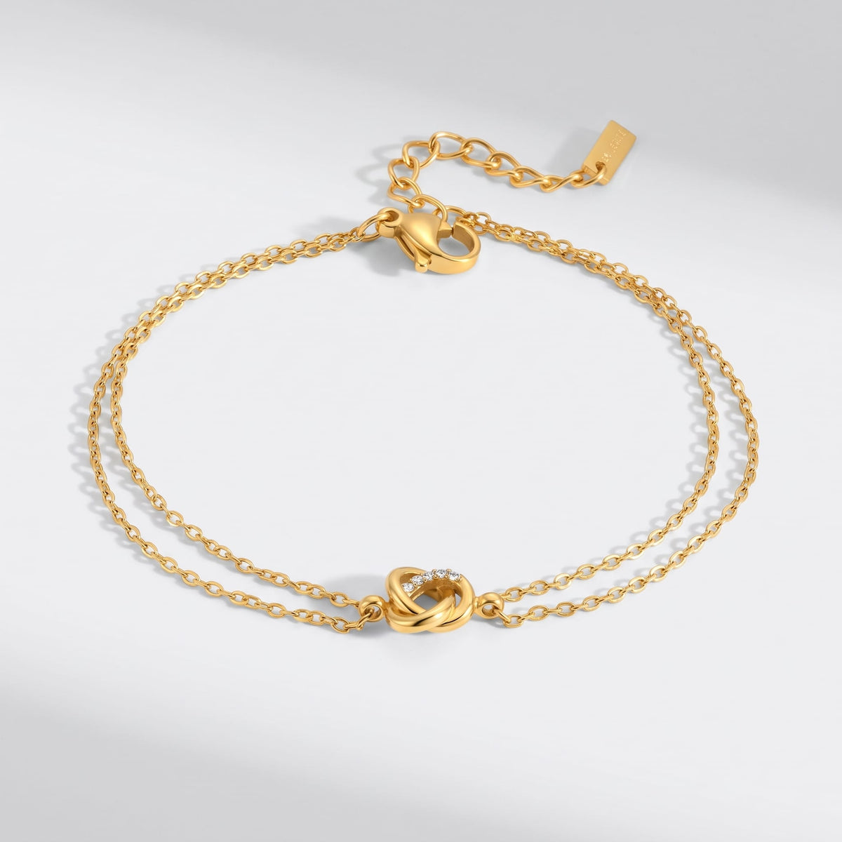 Juliette love knot gold bracelet on a plain white surface displaying its delicate double chain link