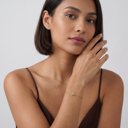 Woman wearing the Juliette love knot gold bracelet on the wrist while posing in a brown top
