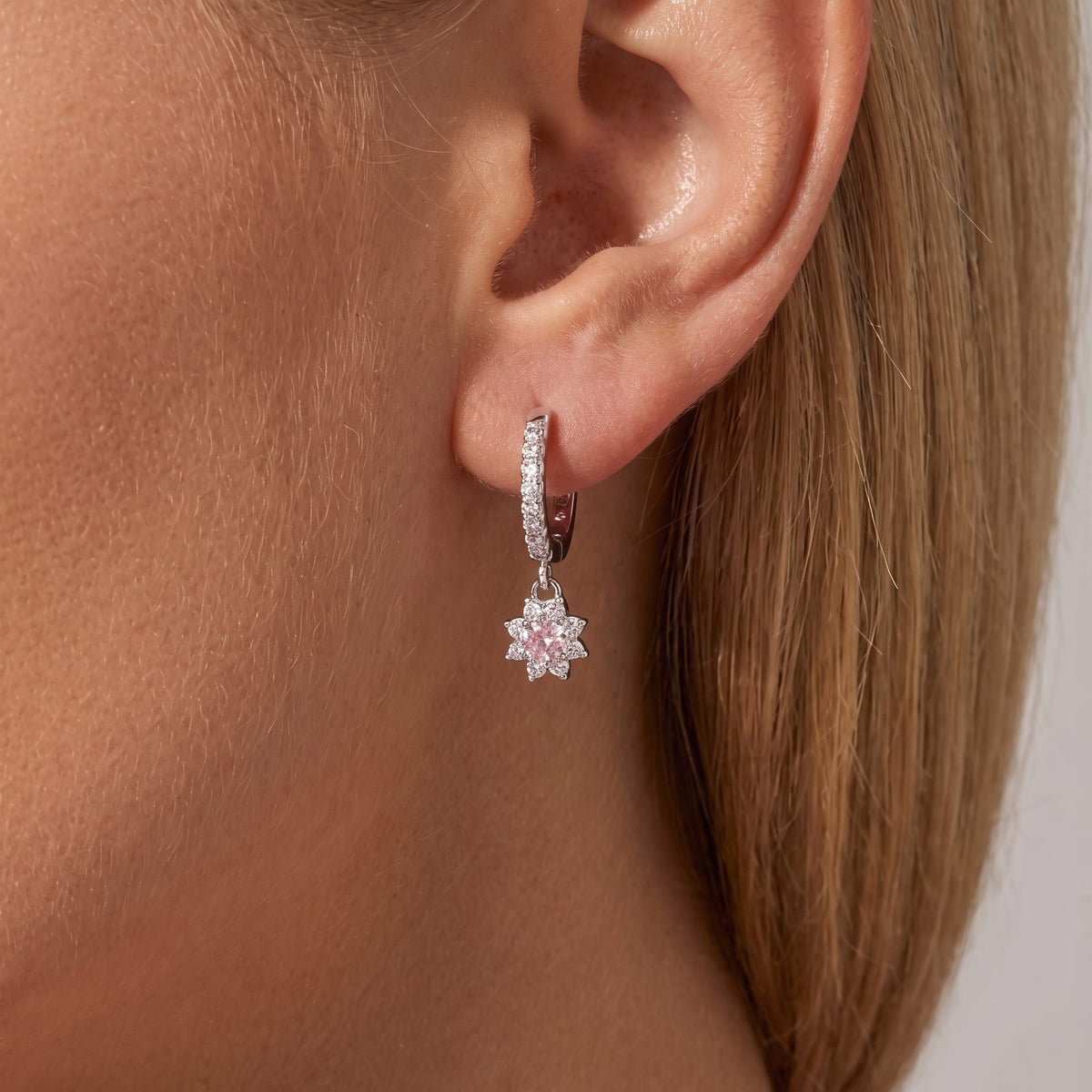 Woman wearing a Juliette silver pavé huggie with a pink crystal flower charm on the ear