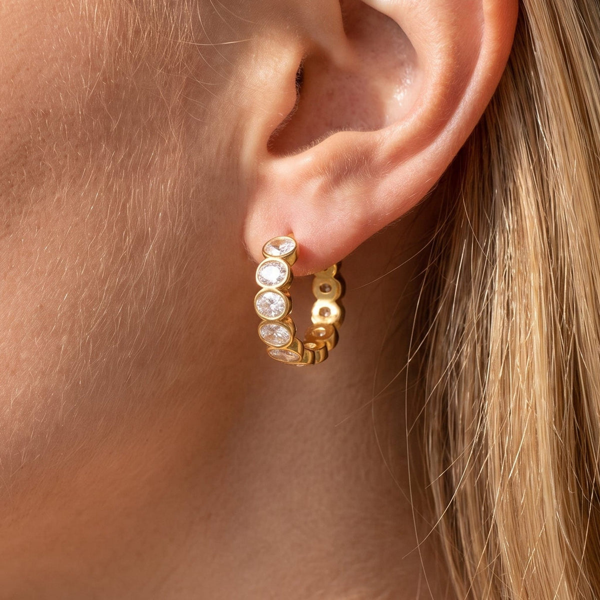 Woman wearing the Léa bezel huggie gold earrings on the ear
