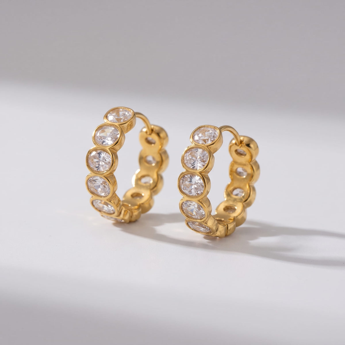 Léa bezel huggie gold earrings on a light gray surface with soft shadows