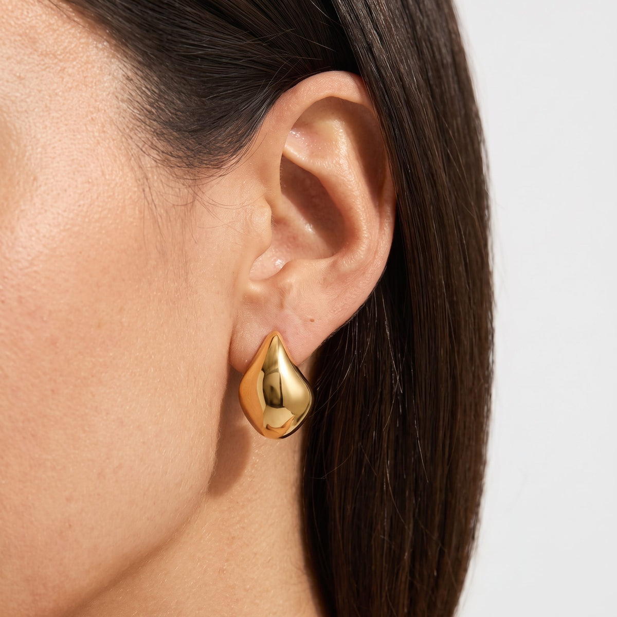 Woman wearing the Lena curved gold hoop, a polished puffed teardrop shape on the ear