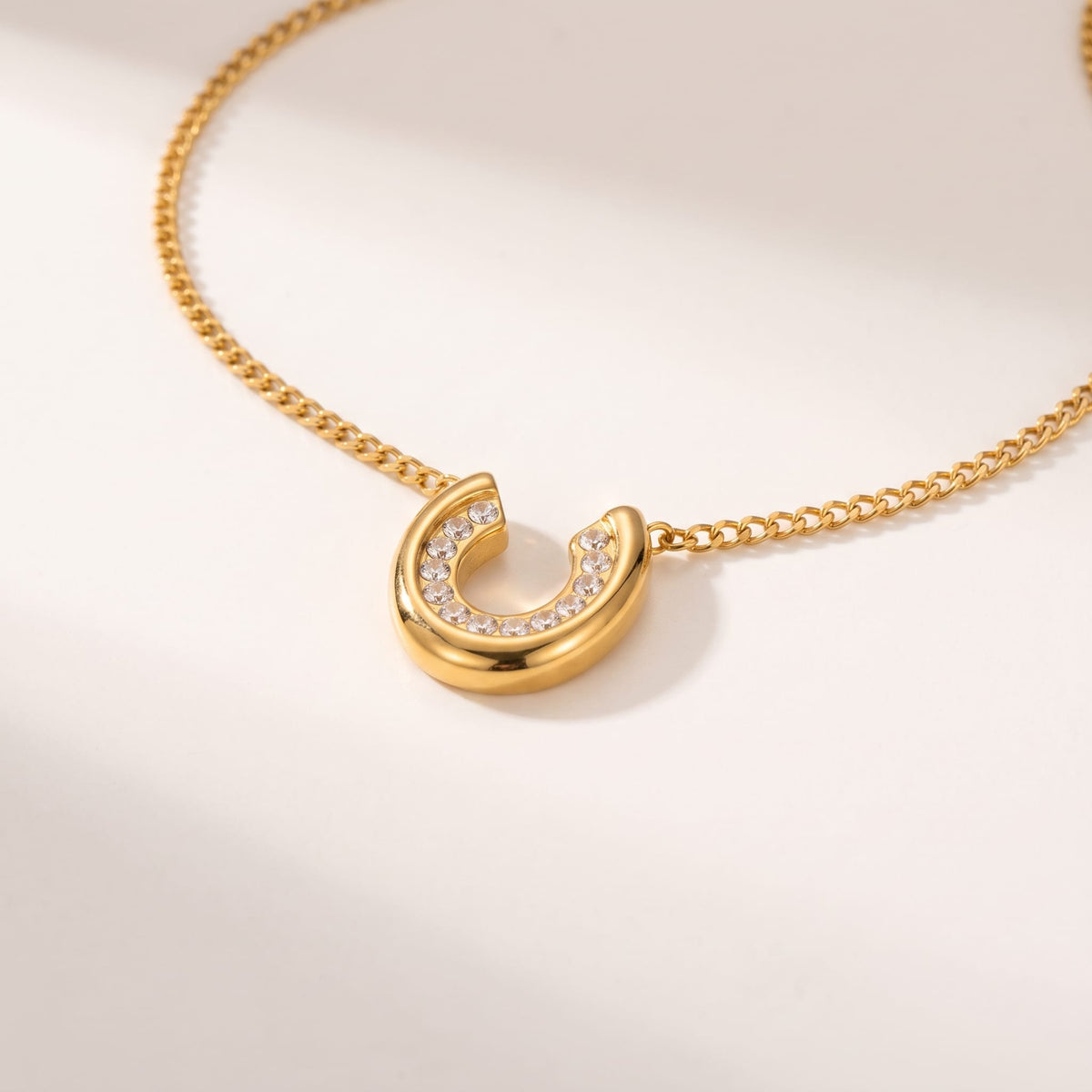 Léonore horseshoe crystal gold necklace on a smooth white surface under soft lighting