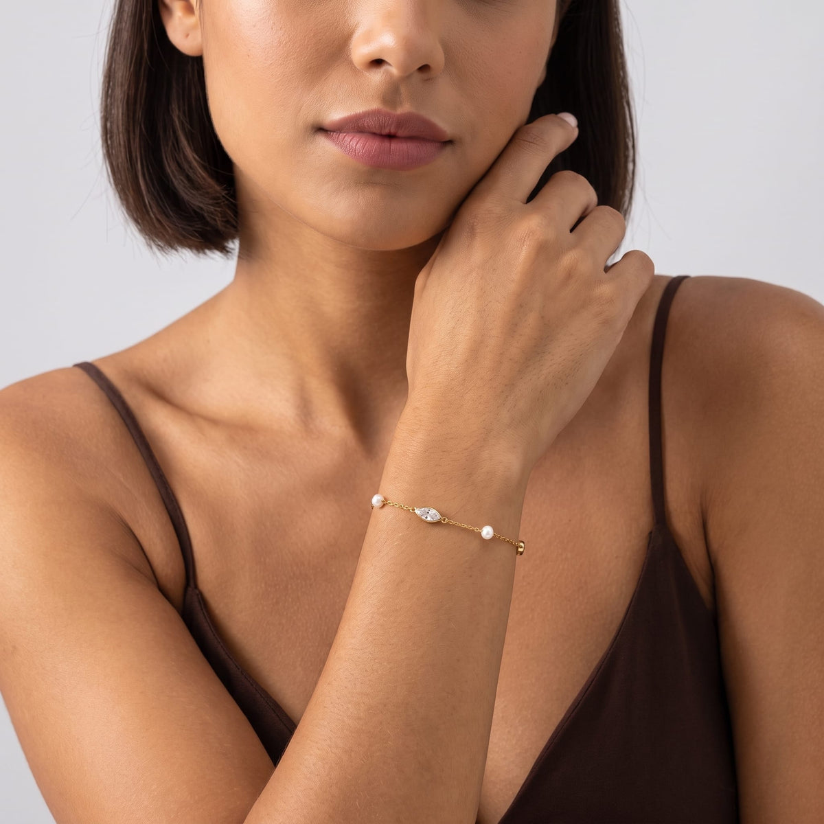 Woman wearing the Liana marquise pearl gold bracelet on the wrist in brown tank top