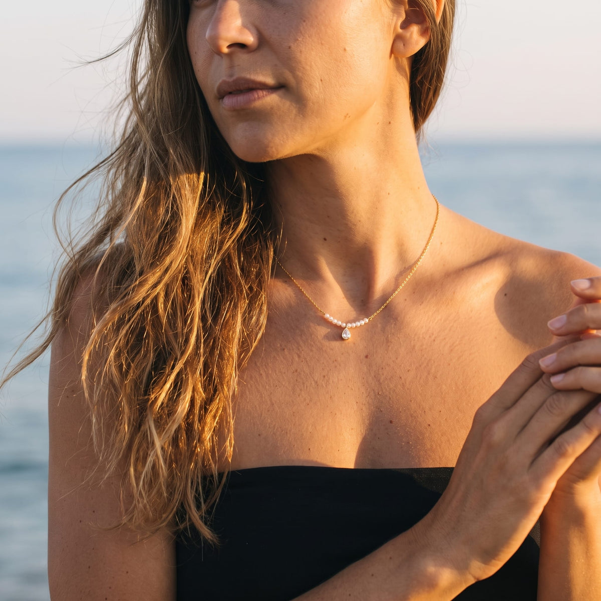 Woman wearing the Lisette pearl bar gold necklace at the collarbone against a sea backdrop