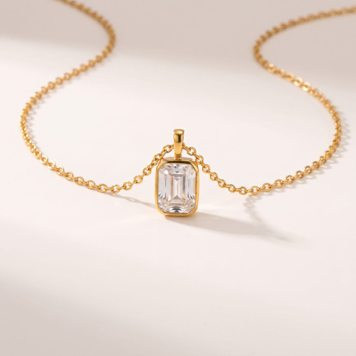 Livia emerald-cut solitaire gold necklace on a plain white surface casting soft shadows