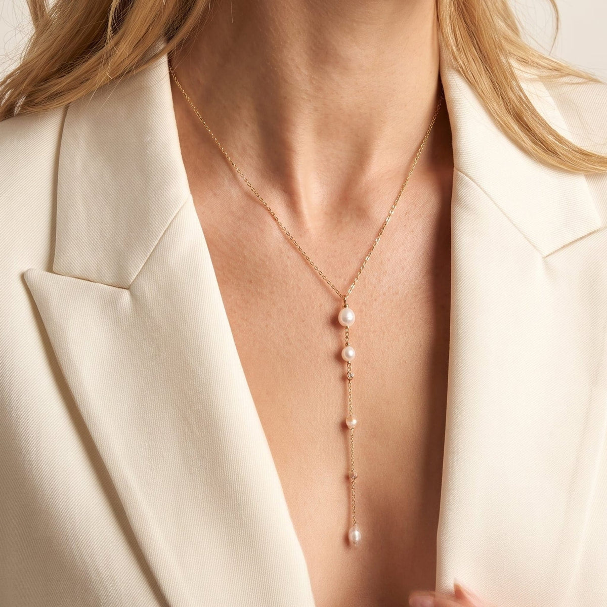 Woman wearing the Livia pearl lariat gold necklace at the collarbone, with a white blazer
