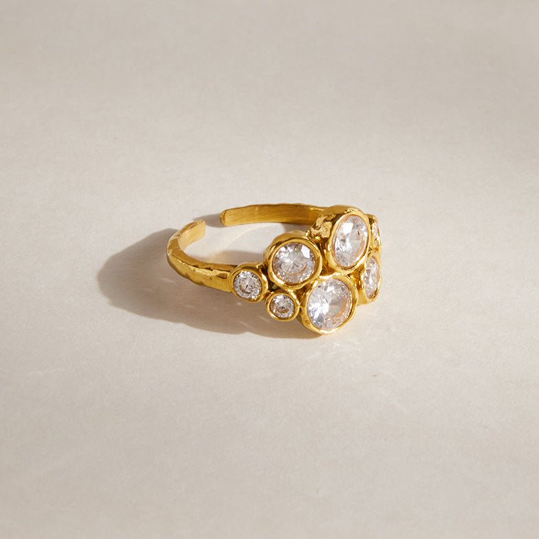 Louise bubble cluster ring resting on a warm beige surface, showing its hammered open band