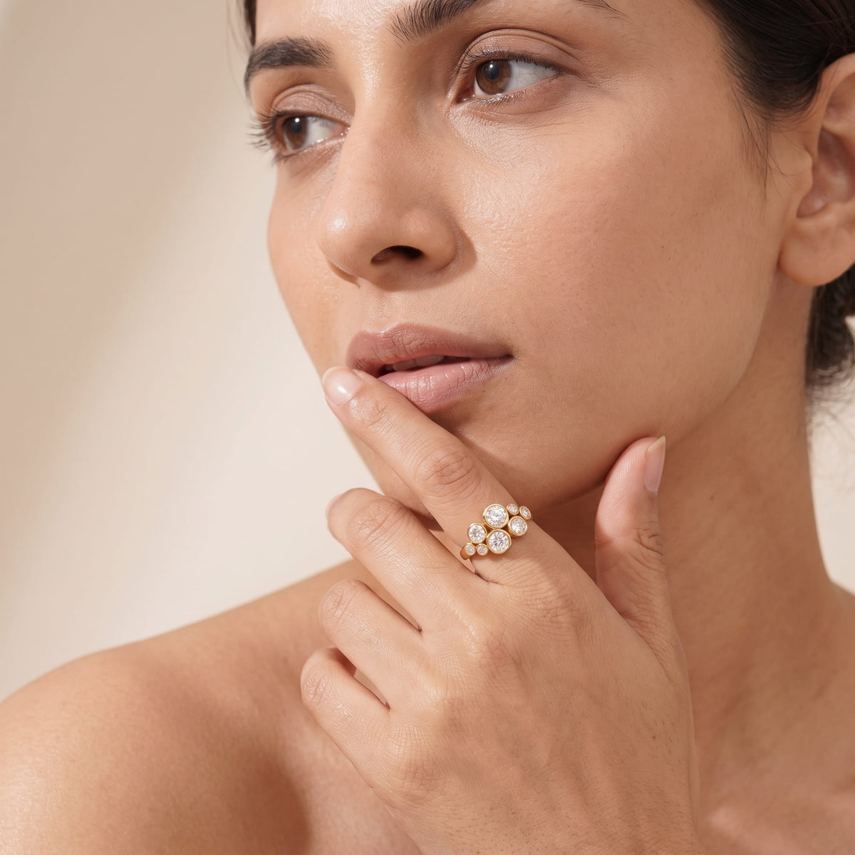 Woman wearing the Louise bubble cluster gold ring on the hand with index finger near her mouth