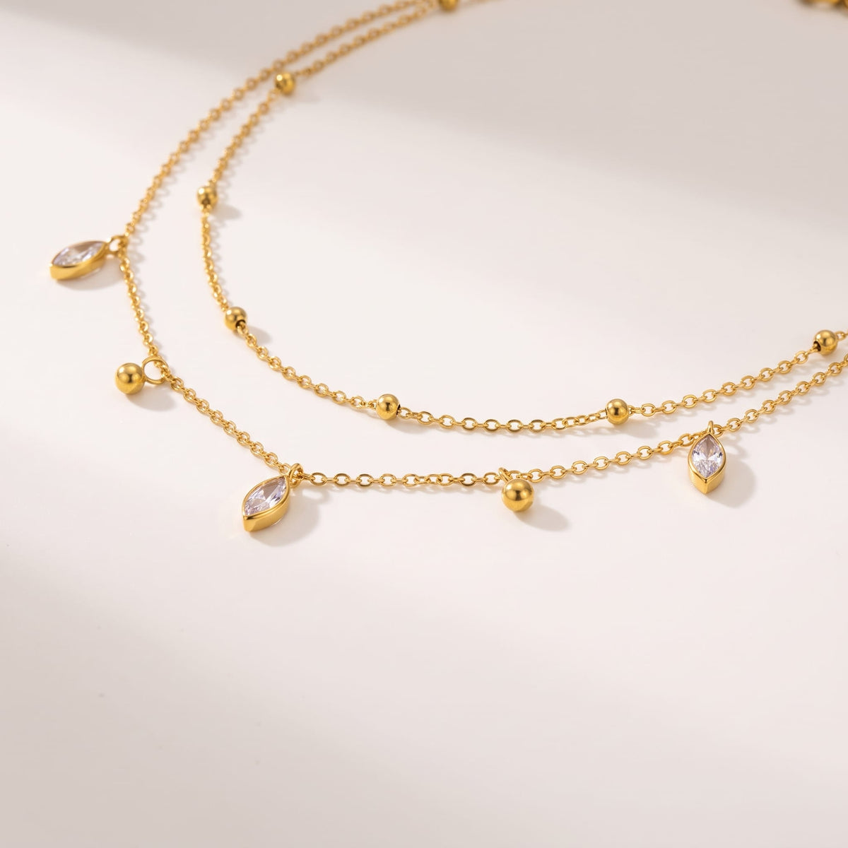 Lucette satellite chain gold necklace on a off-white surface featuring delicate dangling charms