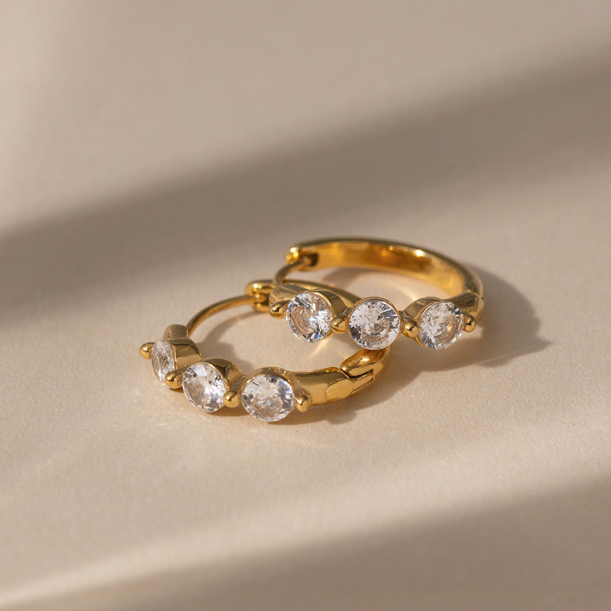 Lucie three-stone huggies lying on a sunlit beige surface, crystals facing up