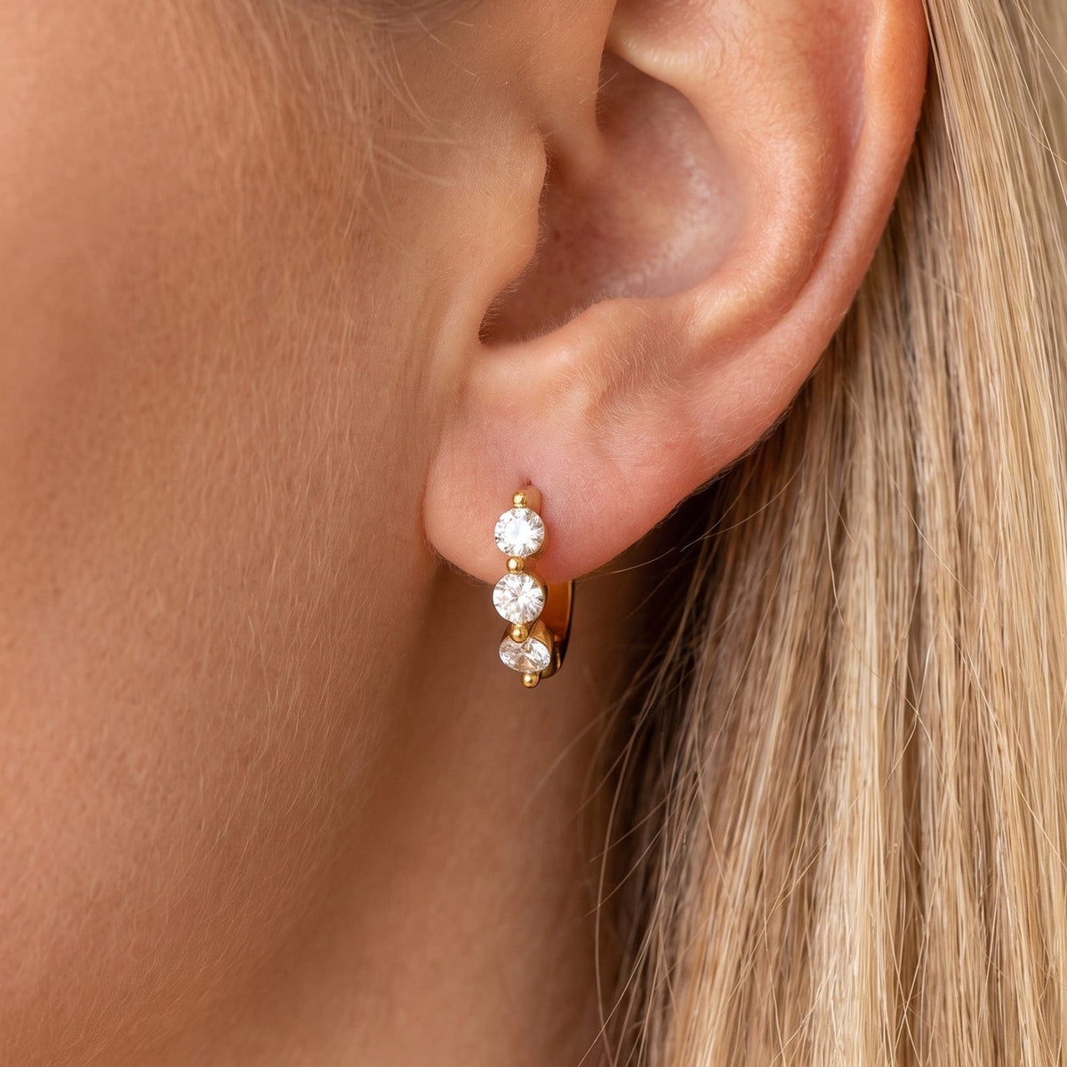 Woman wearing the Lucie three-stone huggie gold earrings on the ear