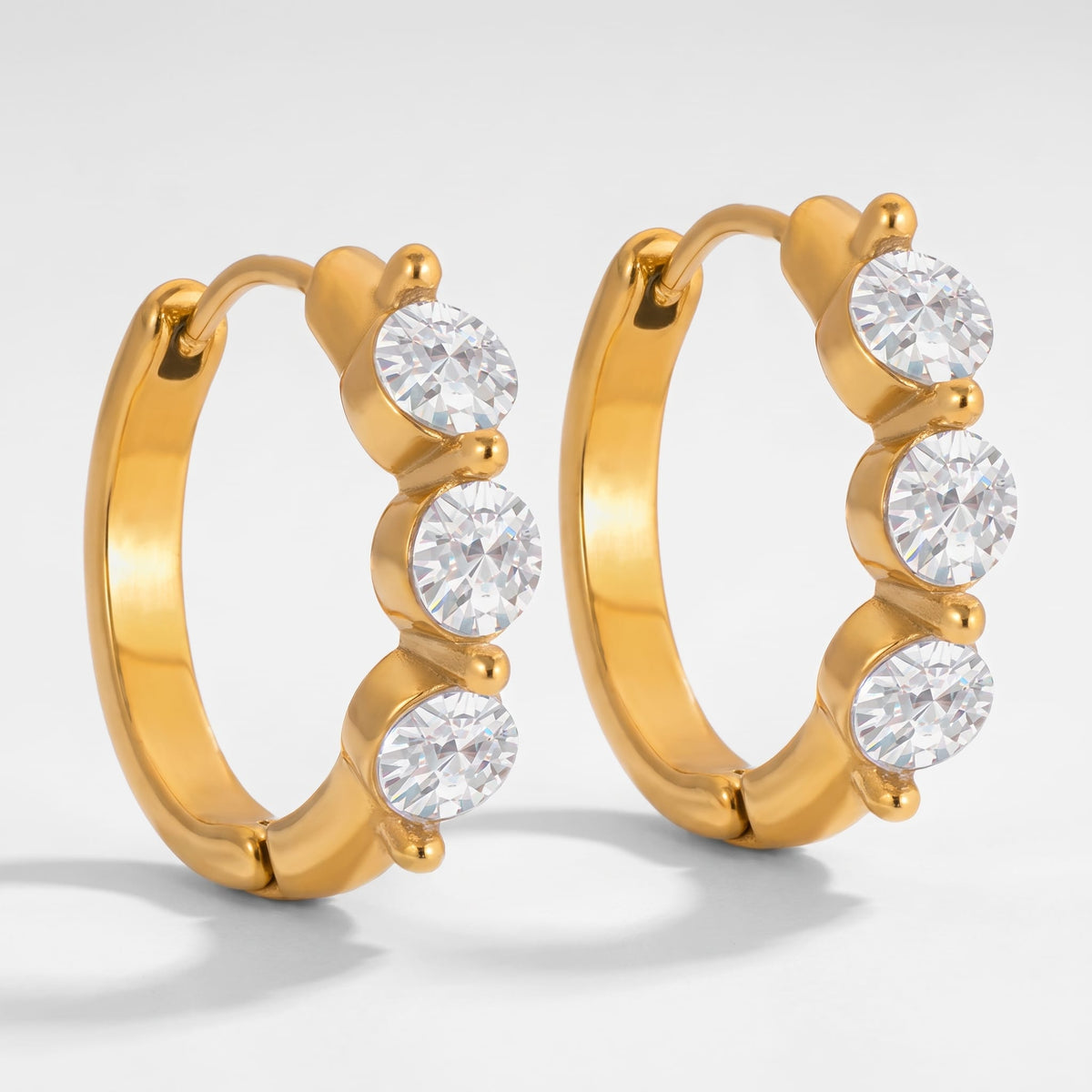Lucie three-stone huggie gold earrings on a plain light background