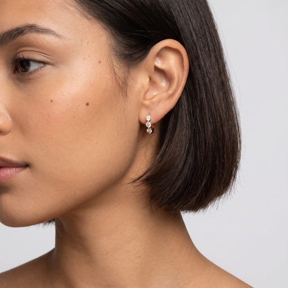 Woman wearing the Lucie three-stone huggie gold earrings on the ear with dark short hair in side profile