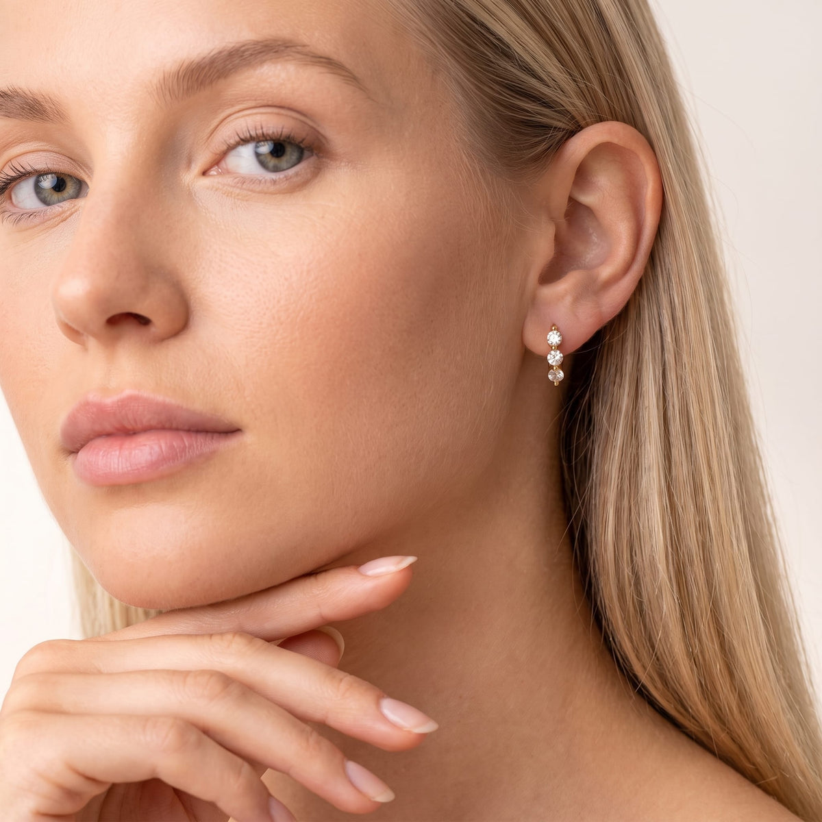 Woman wearing the Lucie three-stone huggie gold earrings on the ear resting her hand near her chin