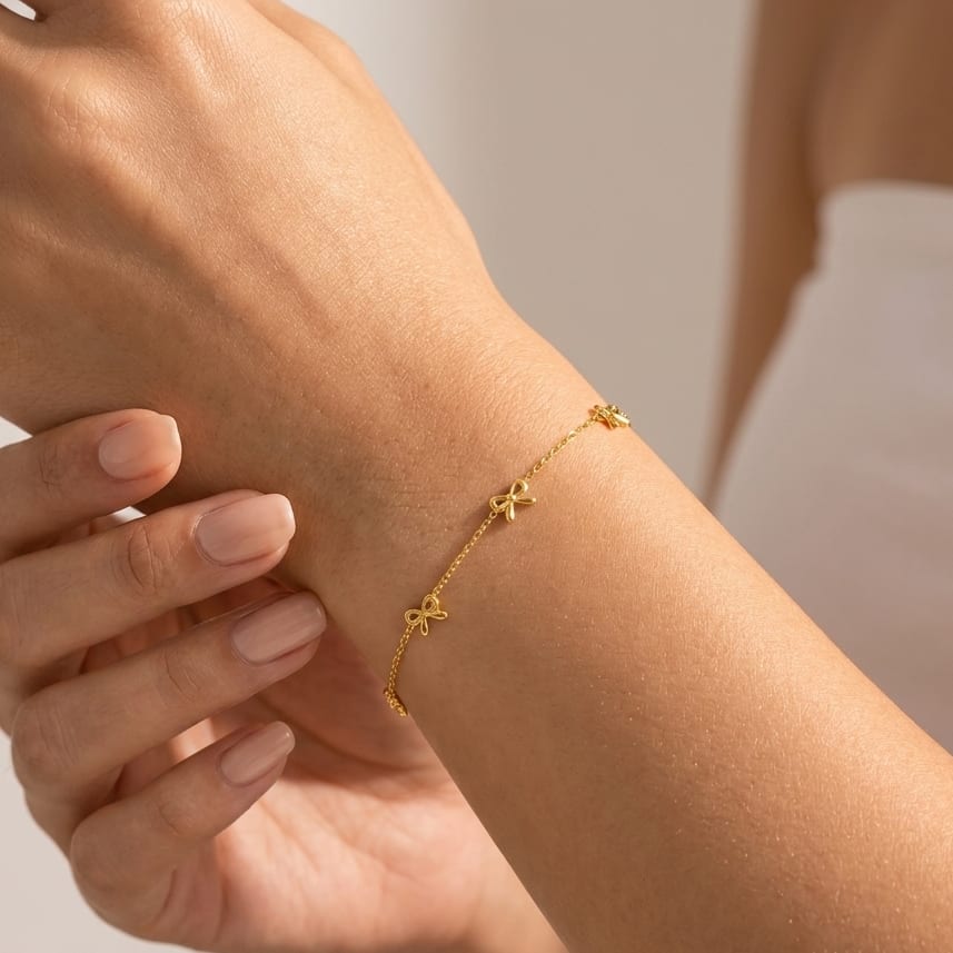 Wider view of a woman wearing the Lucienne gold bow bracelet with small bows spaced along a fine chain