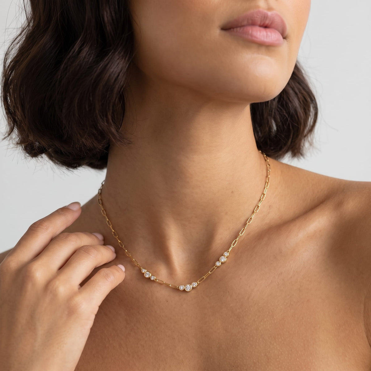 Woman wearing the Lucienne paperclip crystal gold necklace at the collarbone with hand resting near shoulder