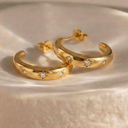 Luna star crescent gold earrings resting on a cream plate in sunlight