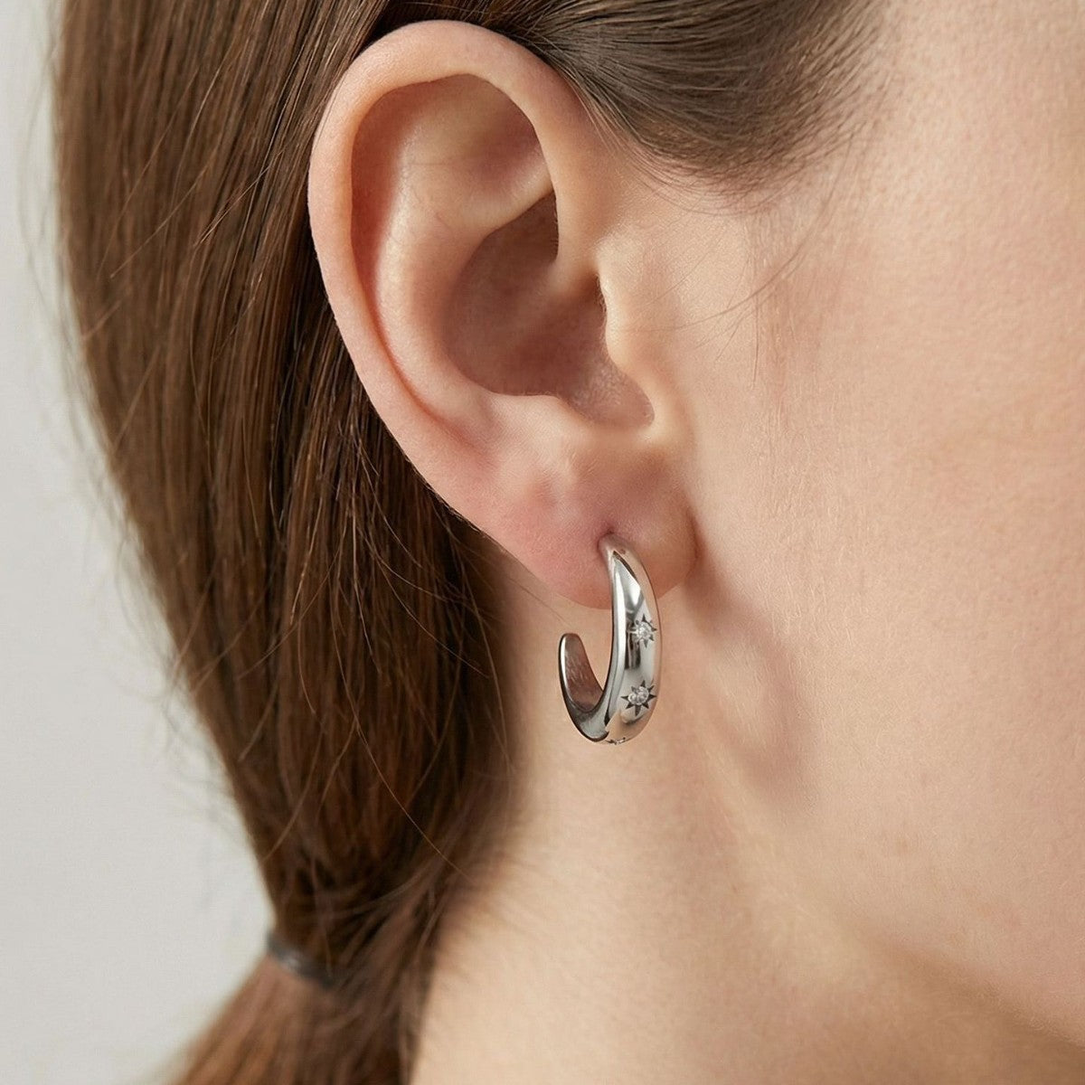 Woman wearing the Luna star crescent silver earring, a polished crescent hoop with tiny star-set crystals
