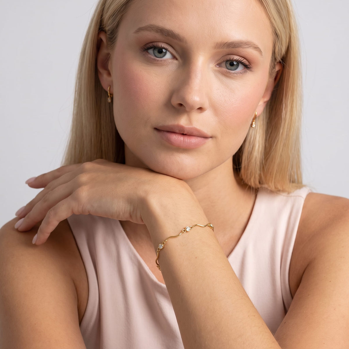 Woman wearing the Luna wave crystal gold bracelet on the wrist resting her chin on hand