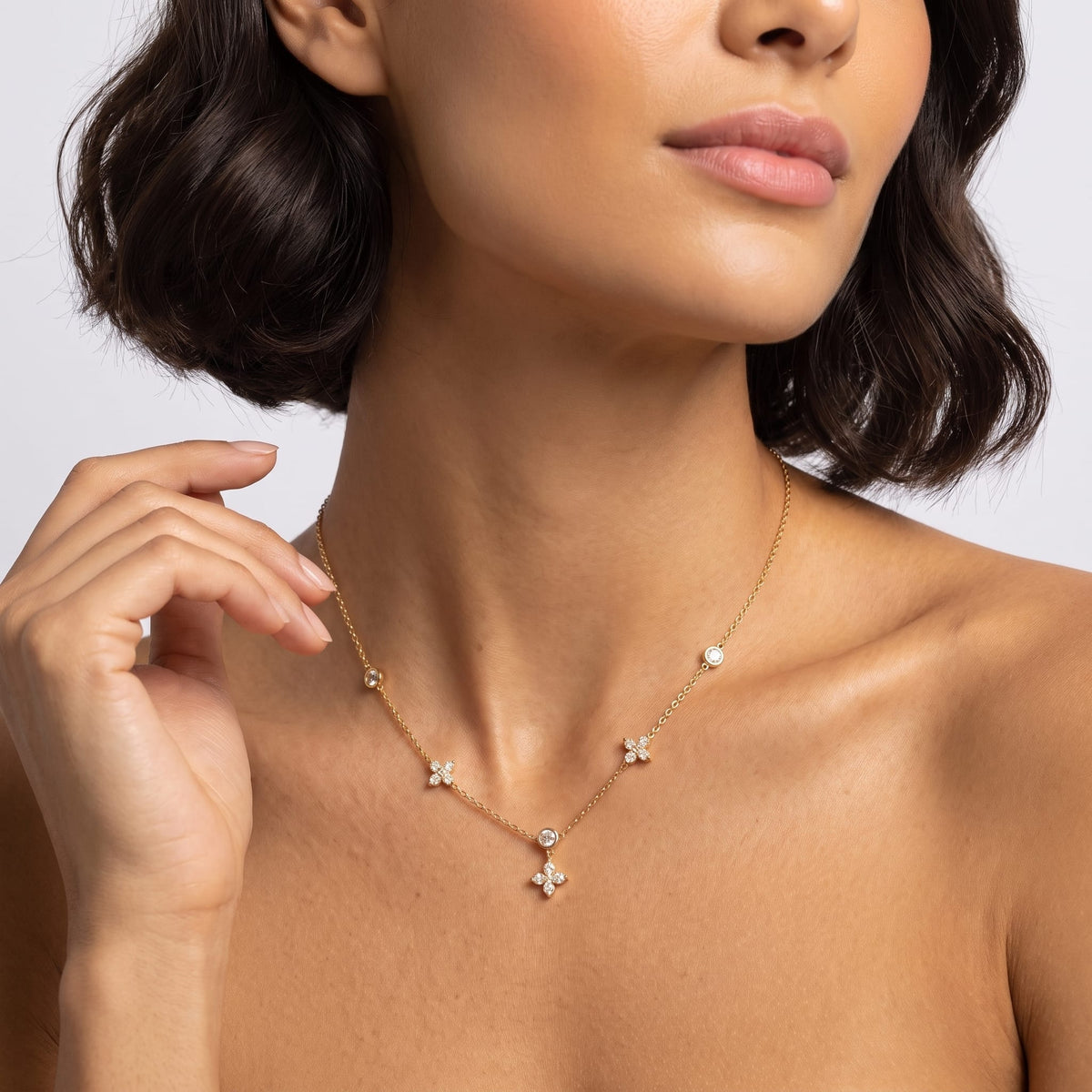 Woman wearing the Madeleine flower station gold necklace at the collarbone touching her dark bob