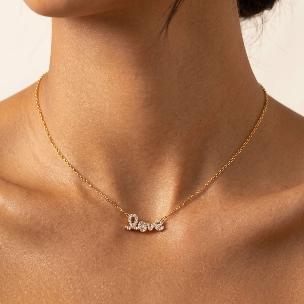 Woman wearing the Manon crystal love script gold necklace at the collarbone