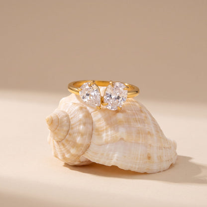 Manon pear duo gold ring on a seashell resting on a beige background