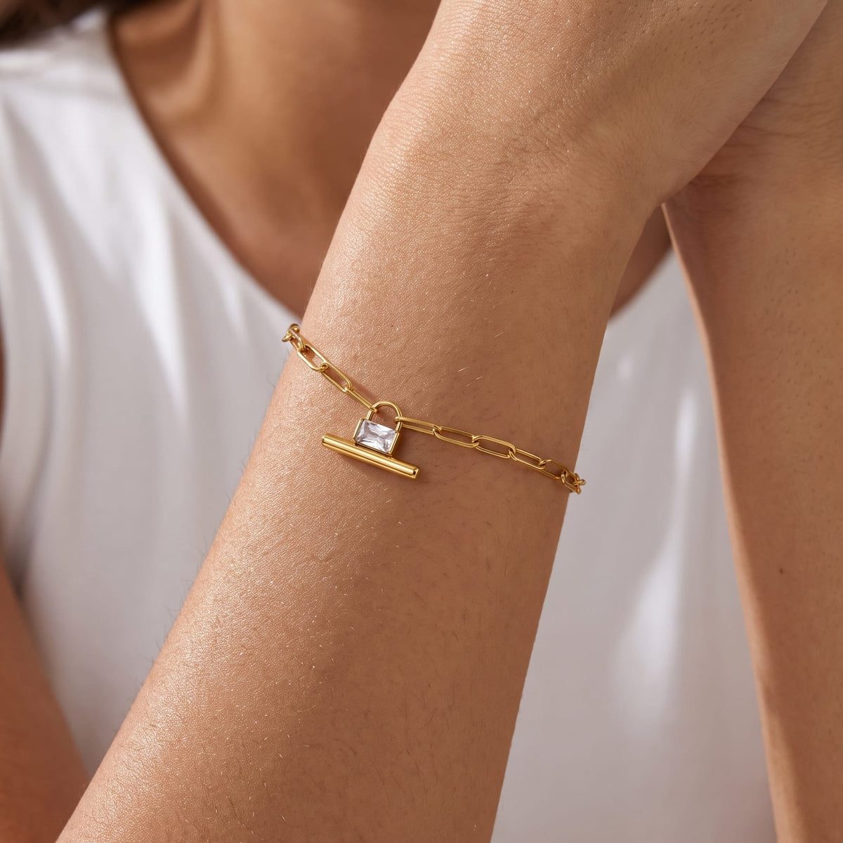 Woman wearing the Margaux padlock t-bar gold bracelet on her wrist with hands folded