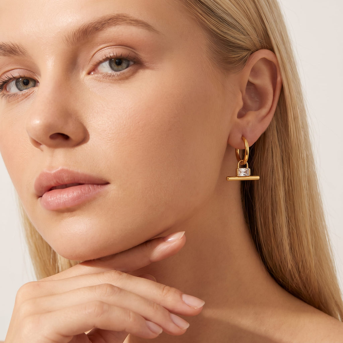 Woman wearing the Margaux padlock t-bar gold earrings on her ear with hand under chin
