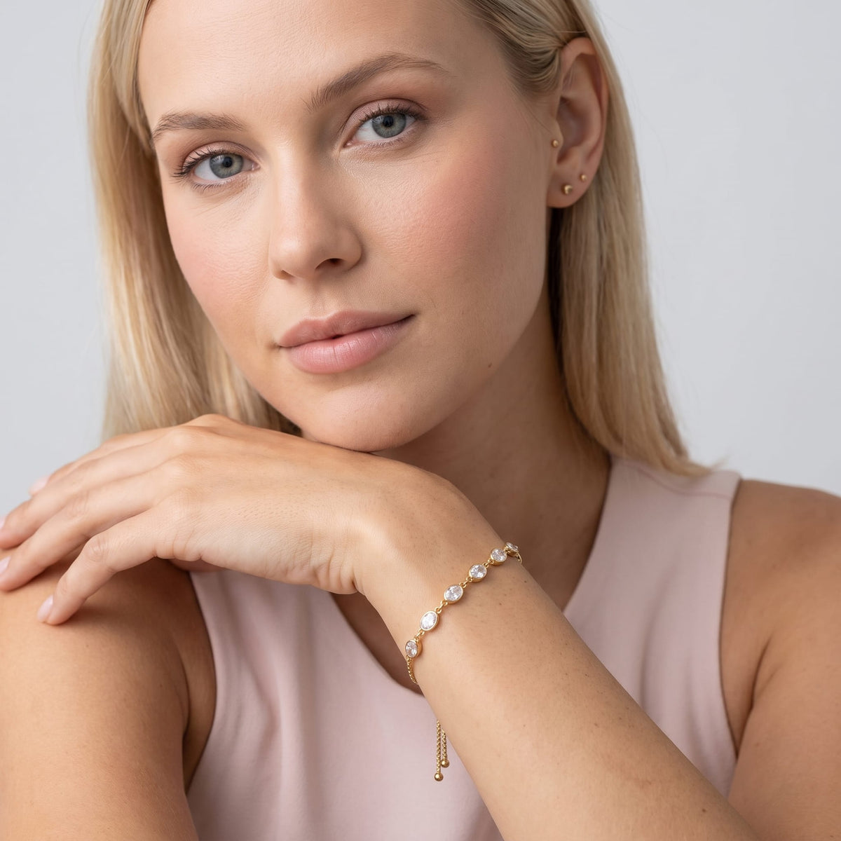 Woman wearing the Marisa oval crystal gold bracelet on the wrist with hand under chin