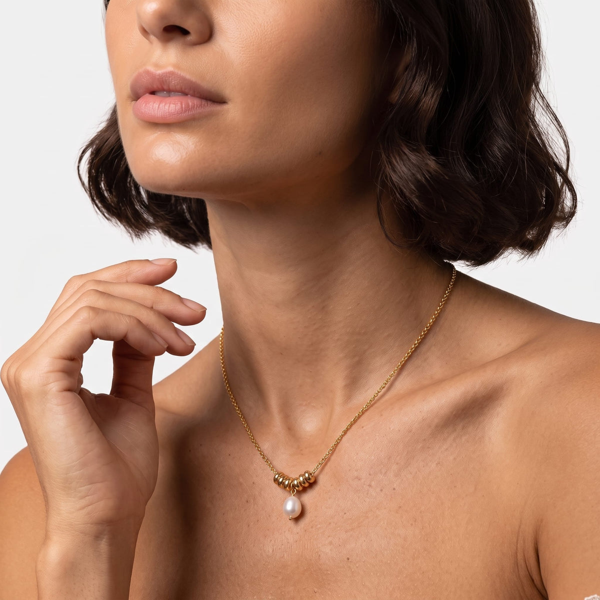Woman wearing the Mathilde pearl drop gold necklace at the collarbone with her hand raised