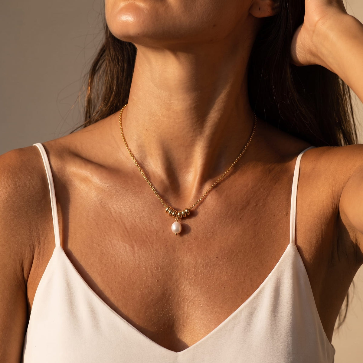 Woman wearing the Mathilde pearl drop gold necklace at the collarbone while wearing a white camisole