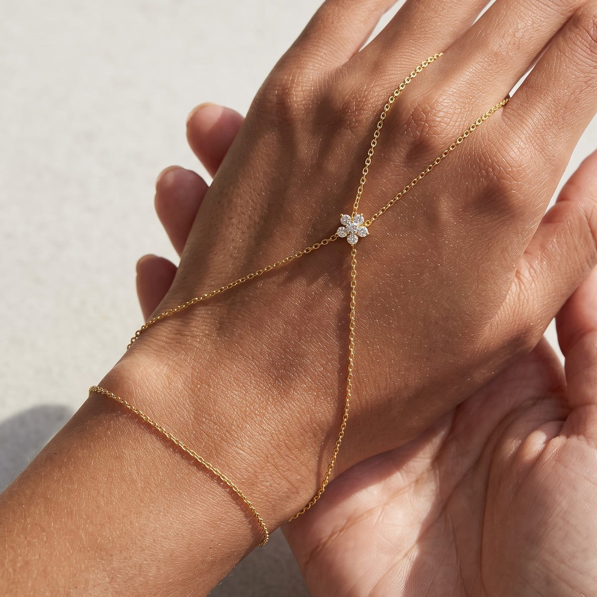 Woman wearing the Mélisa gold hand chain, fine chains meeting at a crystal flower on the back of the hand