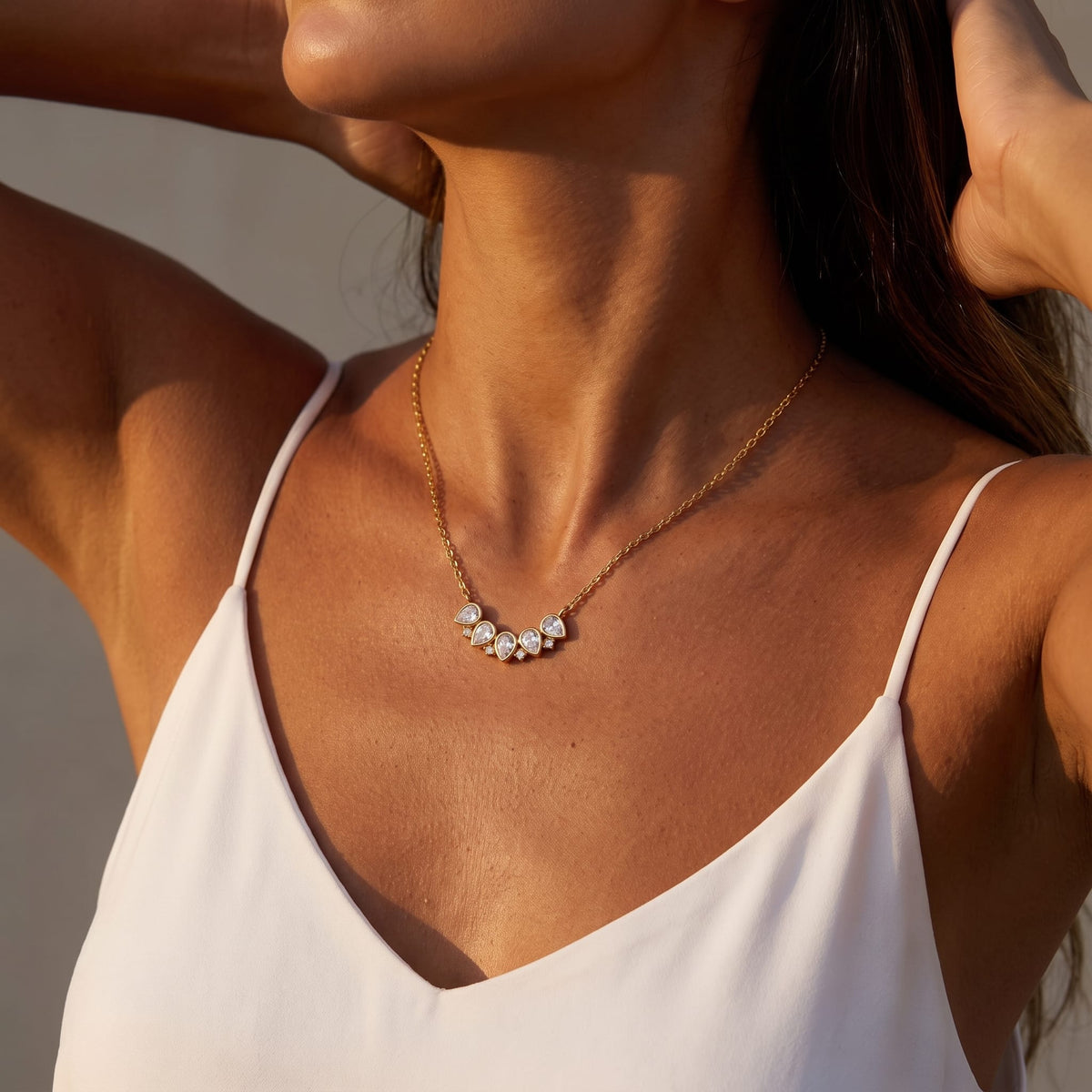 Woman wearing the Mélisande crystal crescent gold necklace at her collarbone with hands behind head