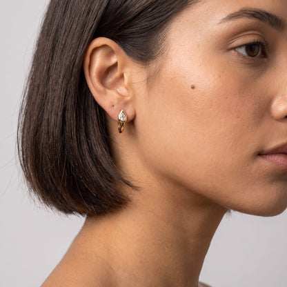 Woman wearing the Mireille pear bezel gold earrings on the ear with a sleek dark bob