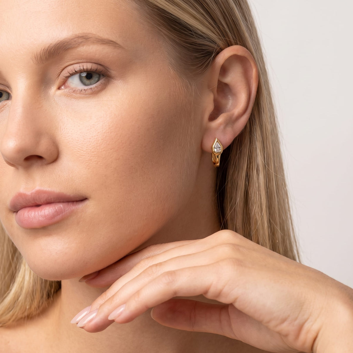 Woman wearing the Mireille pear bezel gold earrings on the ear resting her hand under chin