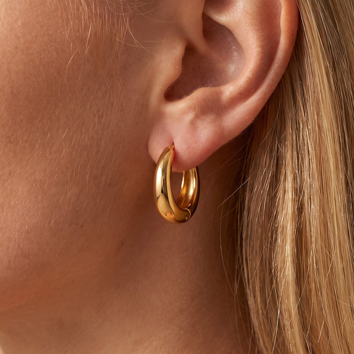 Woman wearing the Nina dome huggie gold earrings on the ear