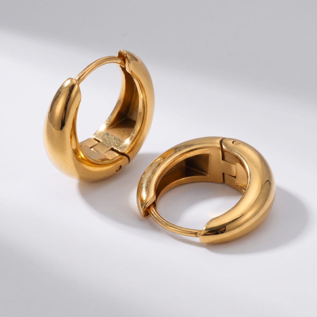Nina dome huggie gold earrings on a white surface with hinged closures open