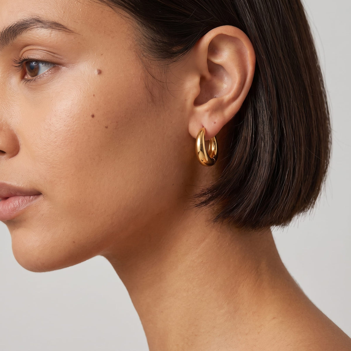 Woman wearing the Nina dome huggie gold earrings on the ear with dark short hair