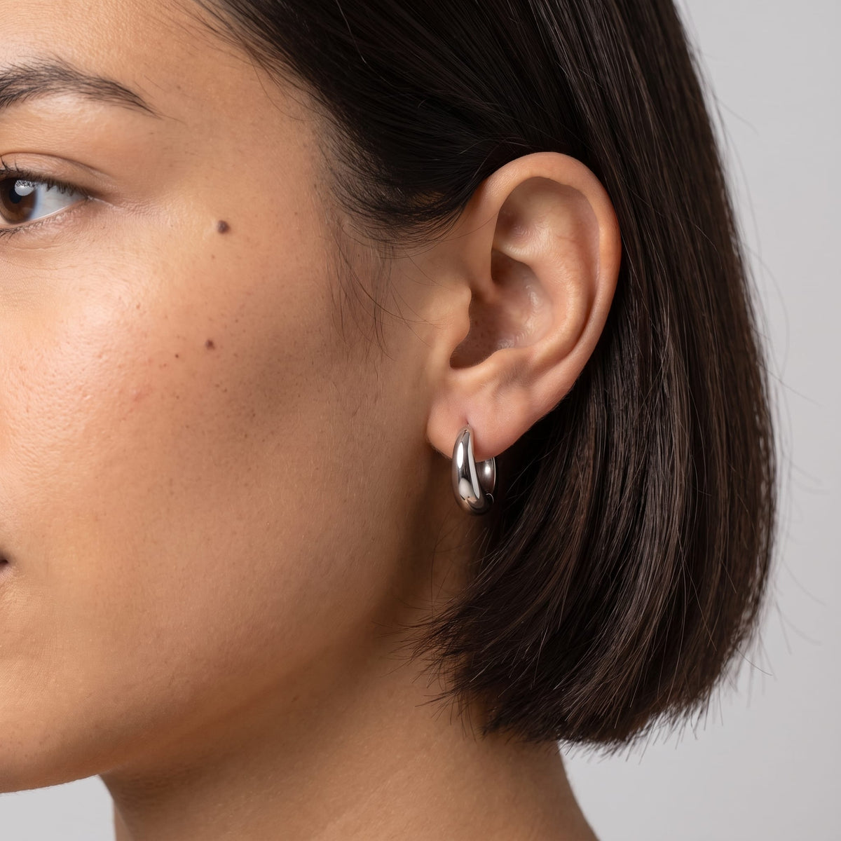 Woman wearing the Nina dome huggie silver earrings on the ear with dark hair
